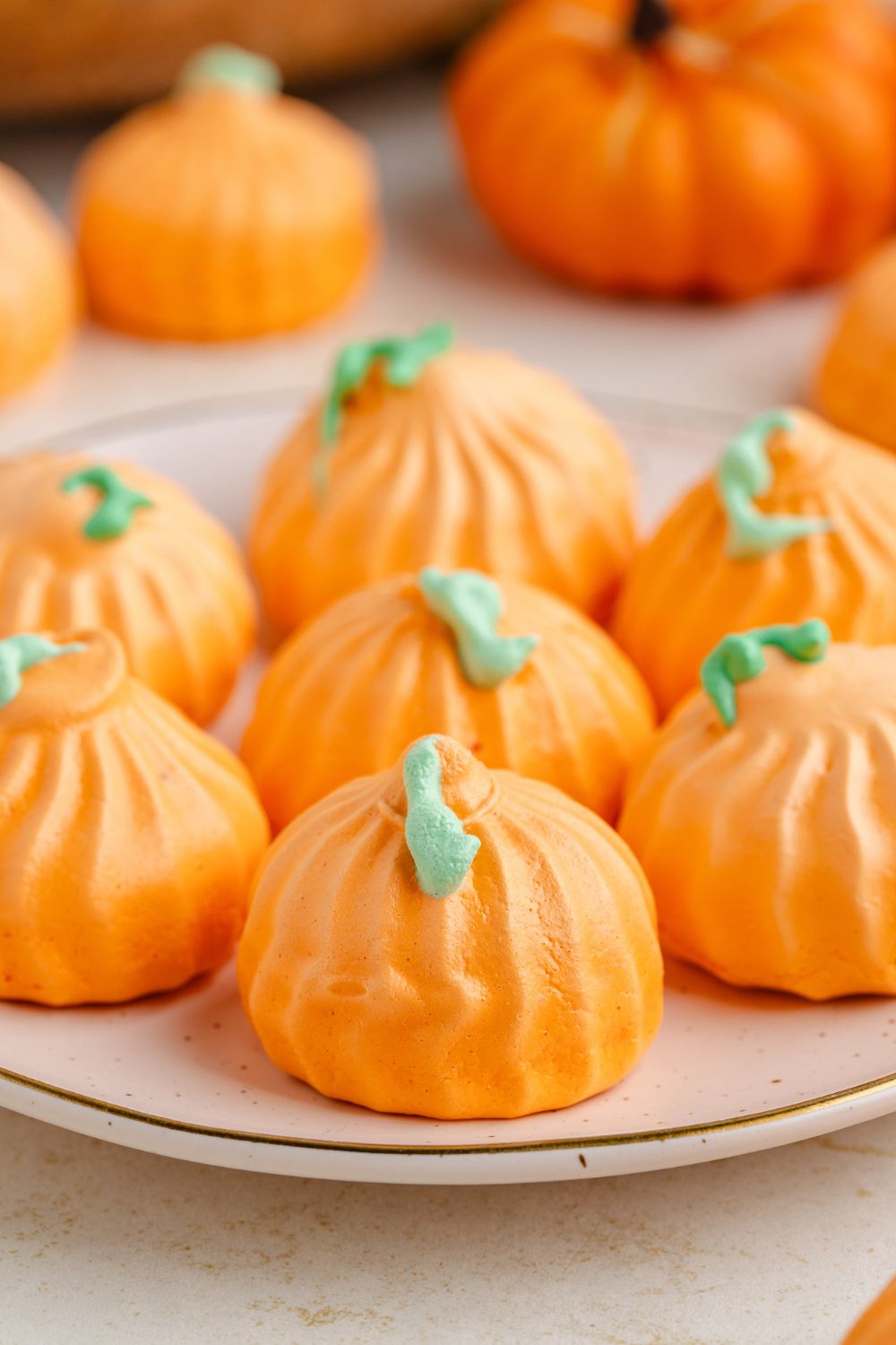 Pumpkin Meringues on a white plate sitting on counter with a few more meringue cookies behind it 