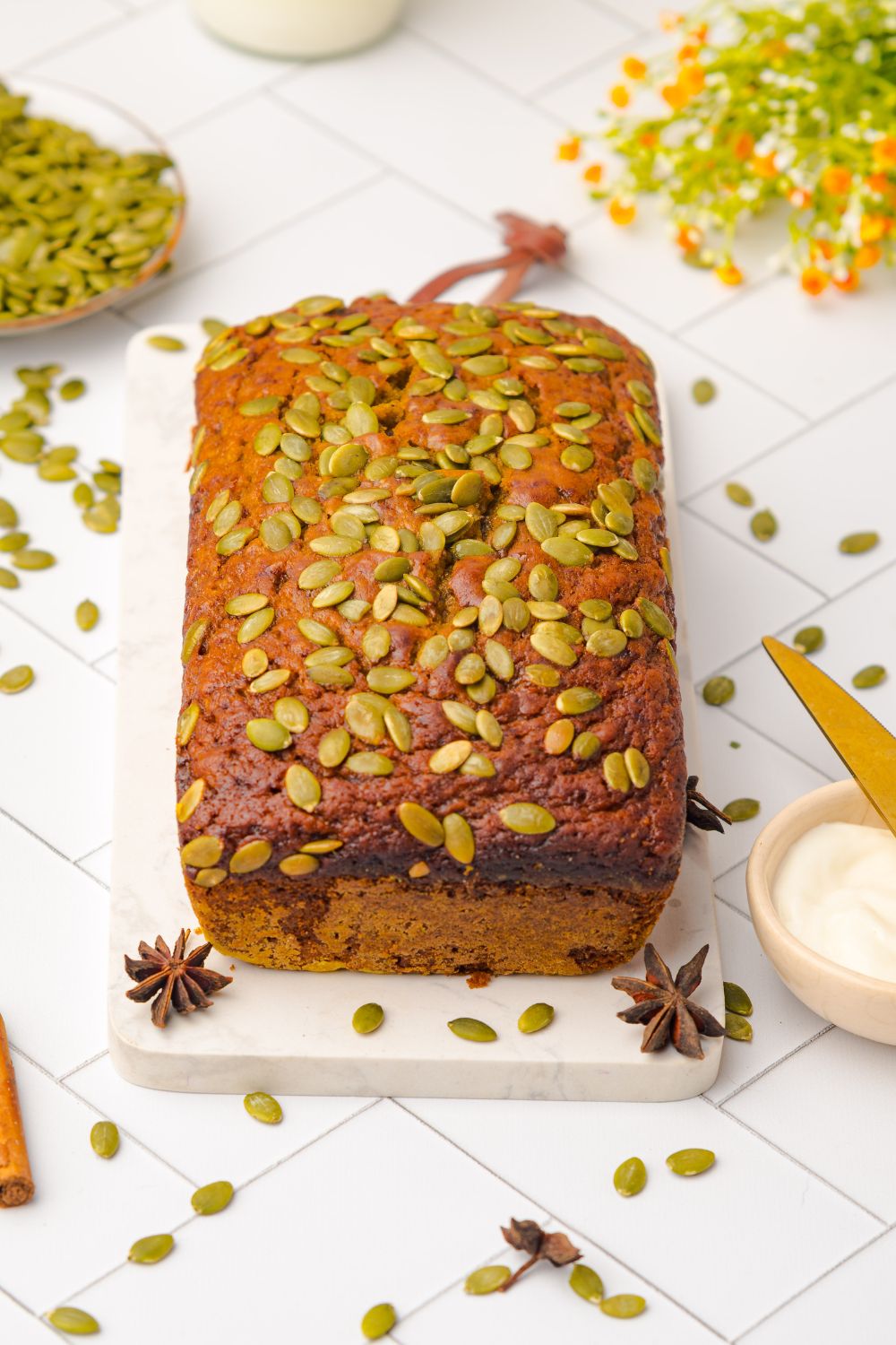 whole loaf of Starbucks Pumpkin Bread on a cutting board on table with seeds and cinnamon sticks scattered around table 