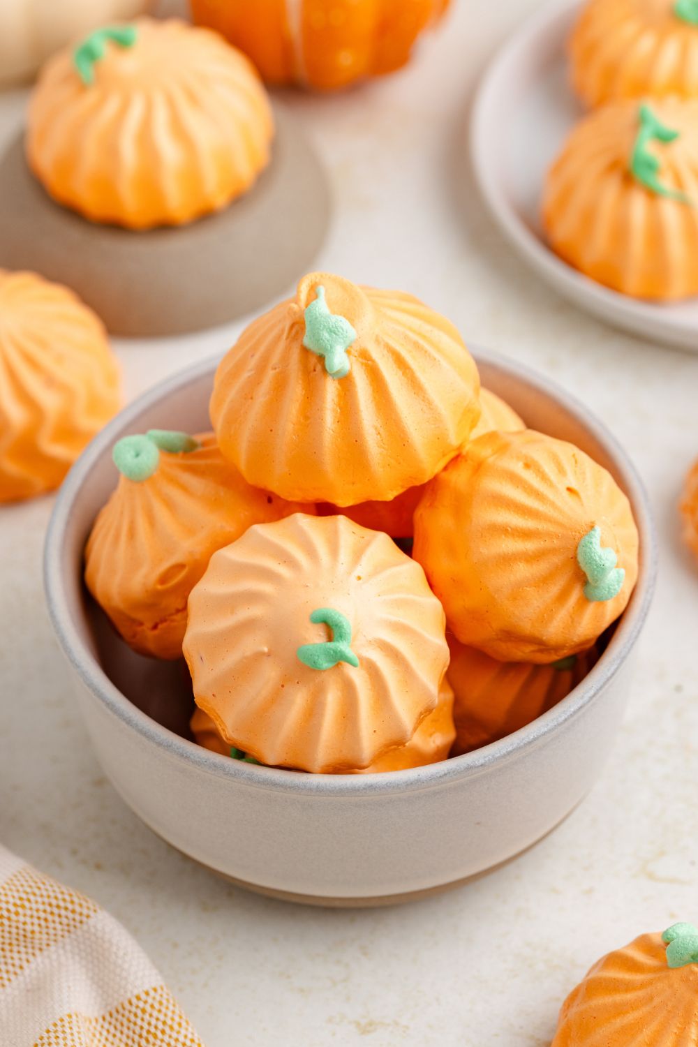 table with Pumpkin Meringue cookies scattered around and a cream bowl full of pumpkin cookies stacked on top of one another 