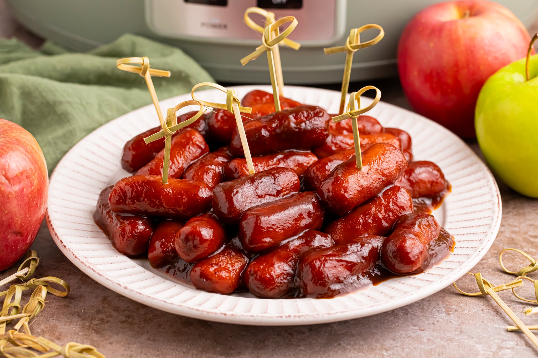 toothpicks in smokies on a white platter with a crockpot sitting behind it 