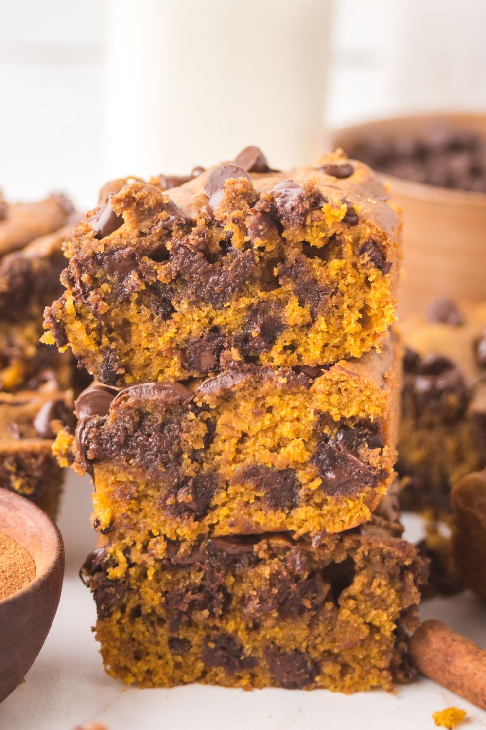 sliced squares of Brown Butter Pumpkin Chocolate Chip Bars stacked on top of one another on white table with more bars around the table 