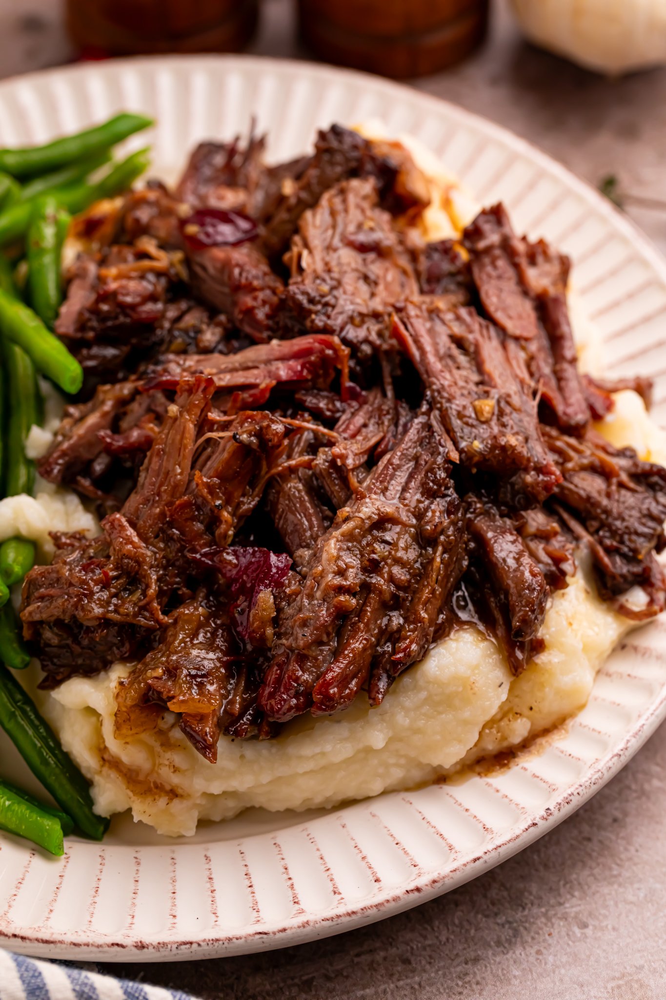 Cranberry Pot Roast shredded on a white plate with mashed potatoes under and a side of green beans 