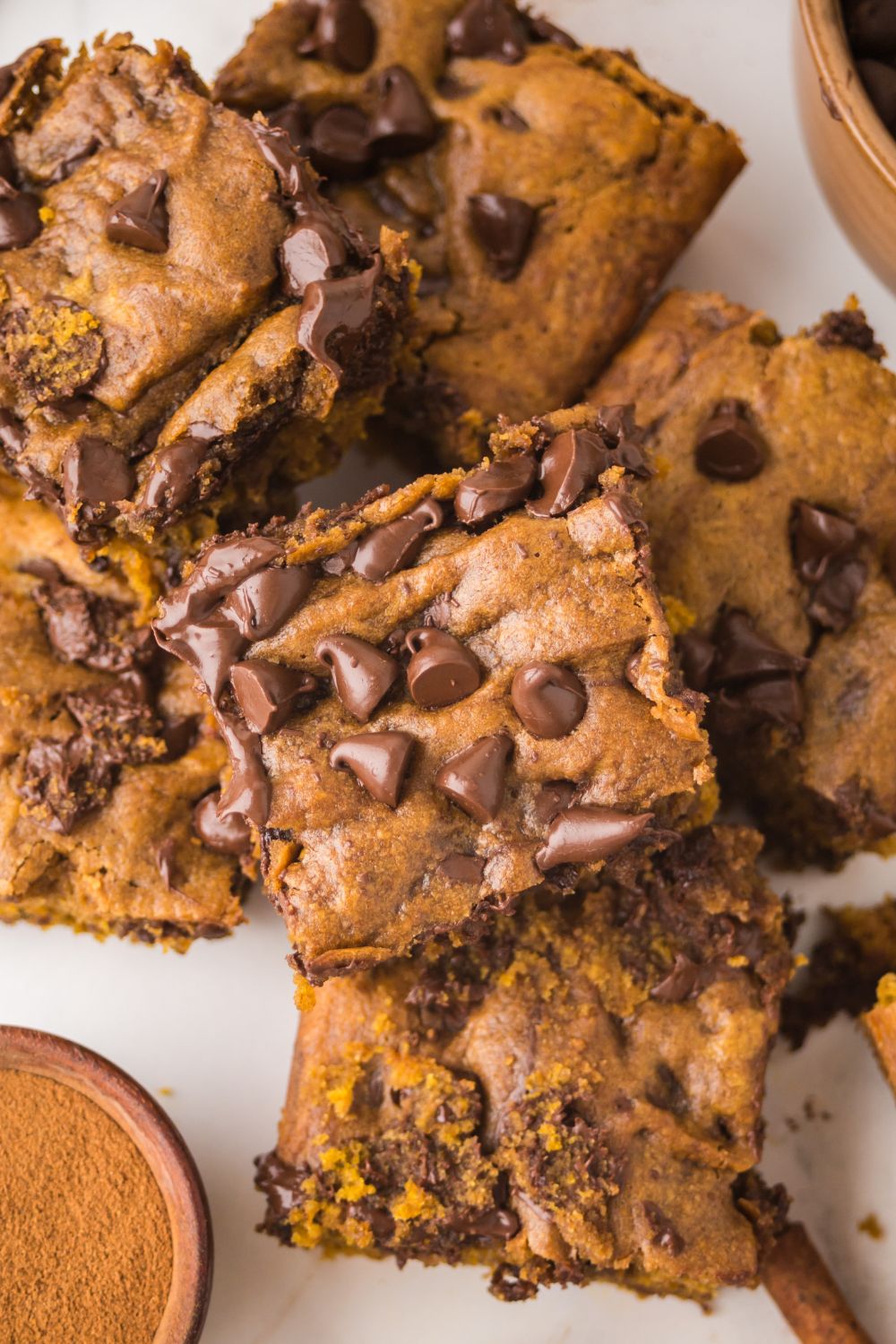 Brown Butter Pumpkin Chocolate Chip Bars stacked on top of one another on a white table 