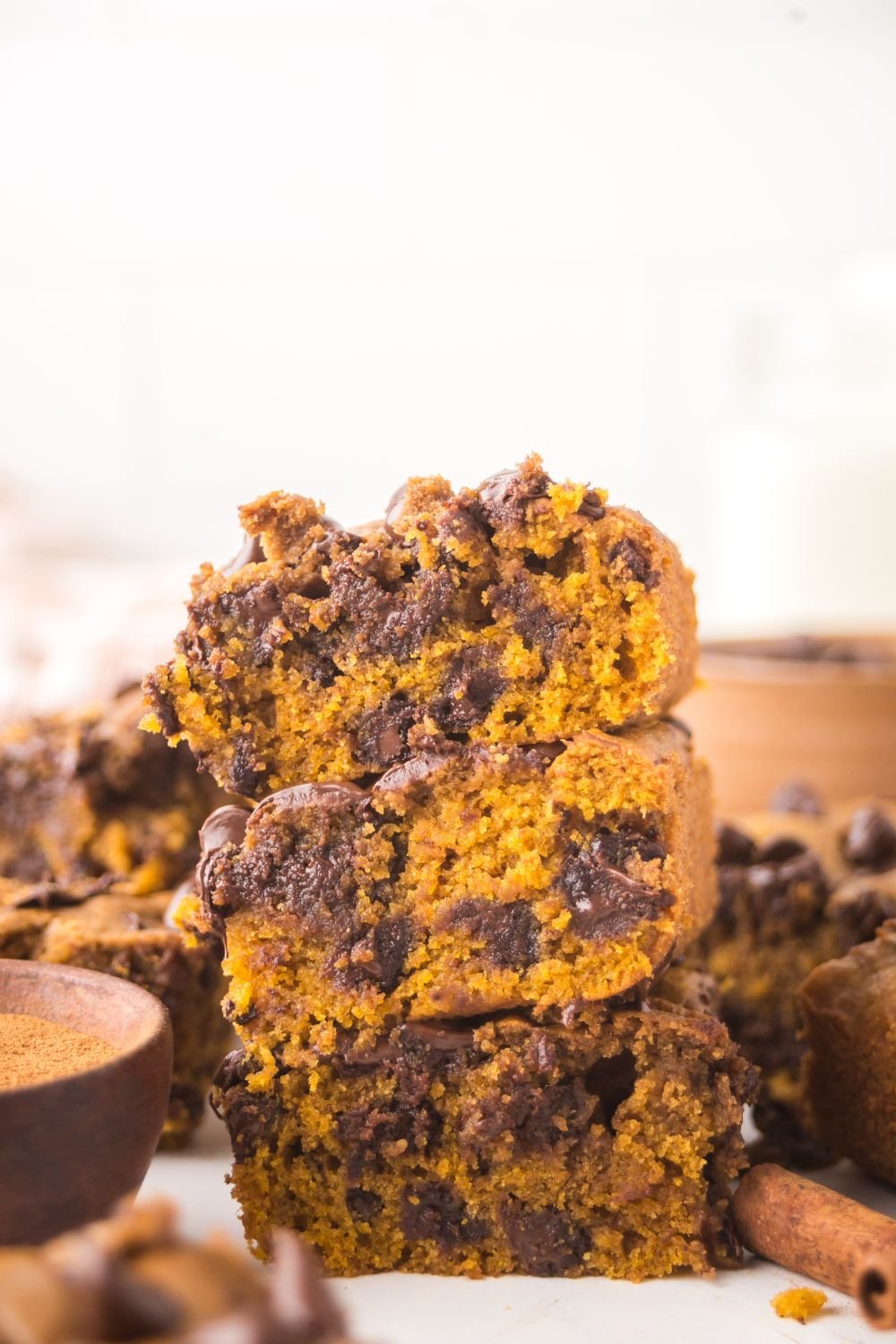 Brown Butter Pumpkin Chocolate Chip Bars stacked on top of one another with more bars placed around the white table 