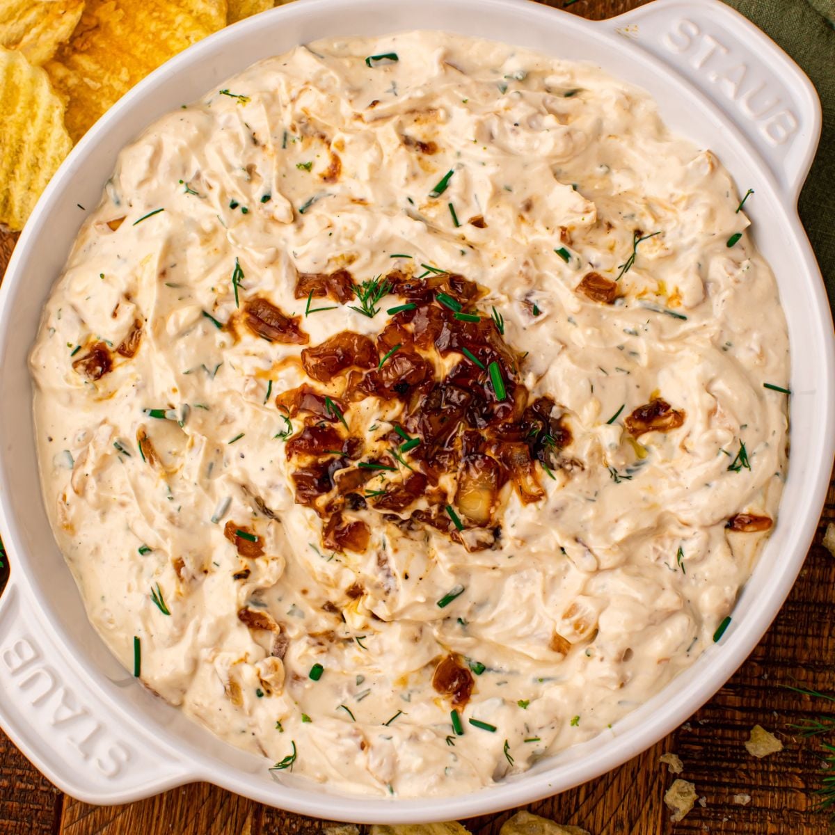 Caramelized Onion Chip Dip in a staub bowl on wooden table with chips to the side 