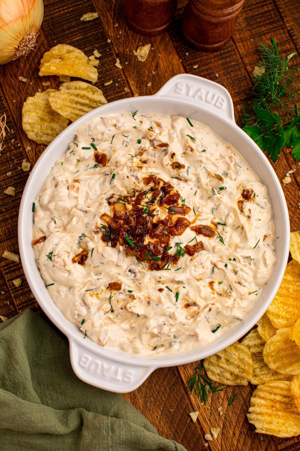 Caramelized Onion Chip Dip in a white bowl on table with chips scattered around the wooden table 