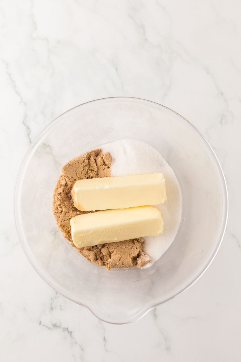 butter and sugars in a glass bowl on marble counter 