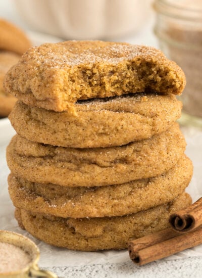 Pumpkin Snickerdoodle Cookies stacked on a white wooden table with a bite missing from the top one
