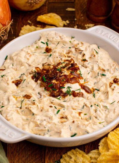Caramelized Onion Chip Dip in a white staub bowl on dark wooden table with chips to the side