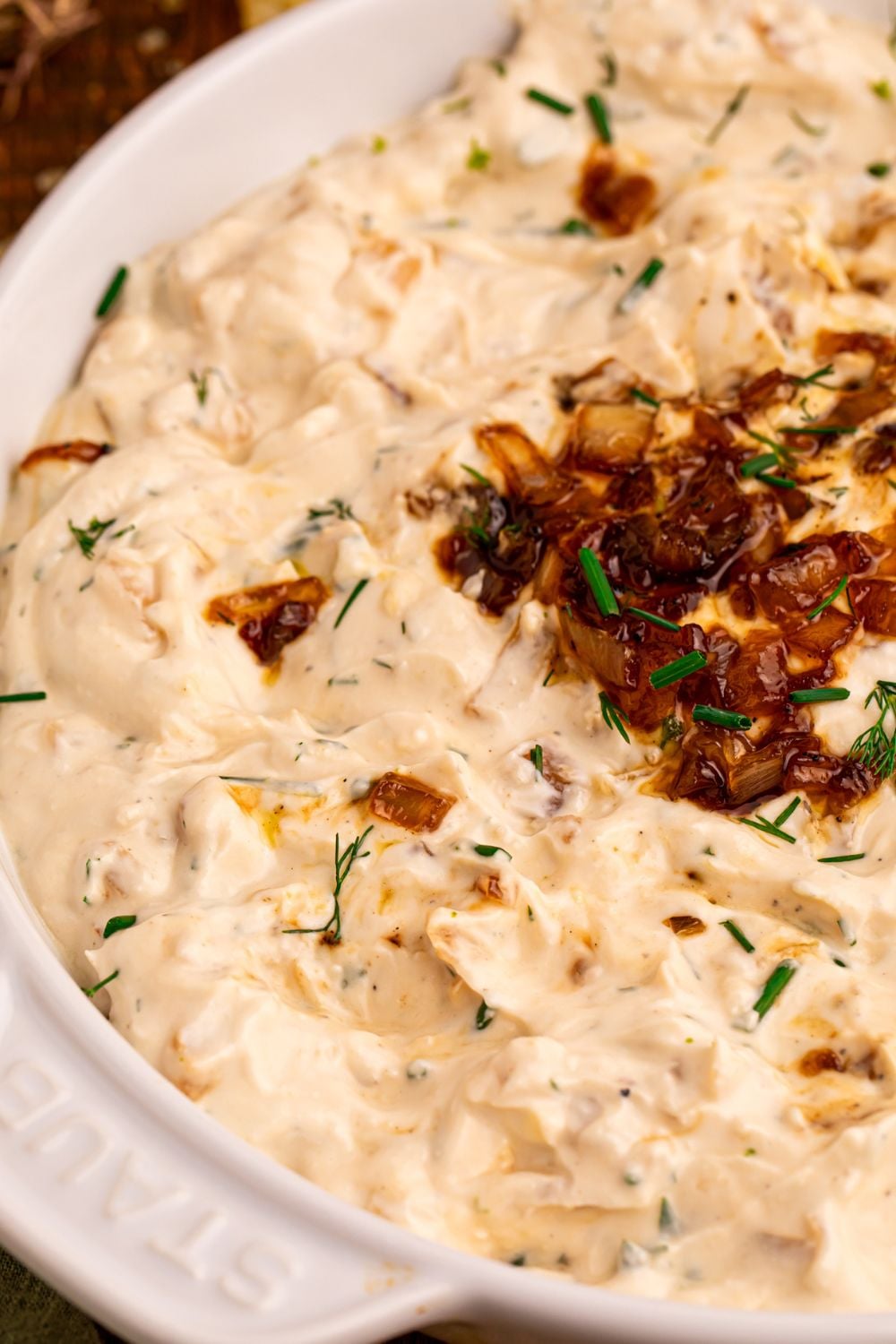 view of a white staub bowl on table with Caramelized Onion Chip Dip inside and a dollop of caramelized onions in the center 