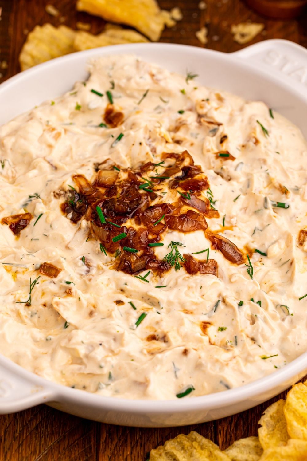 creamy onion dip with caramelized onions on top with chips on a wooden table 