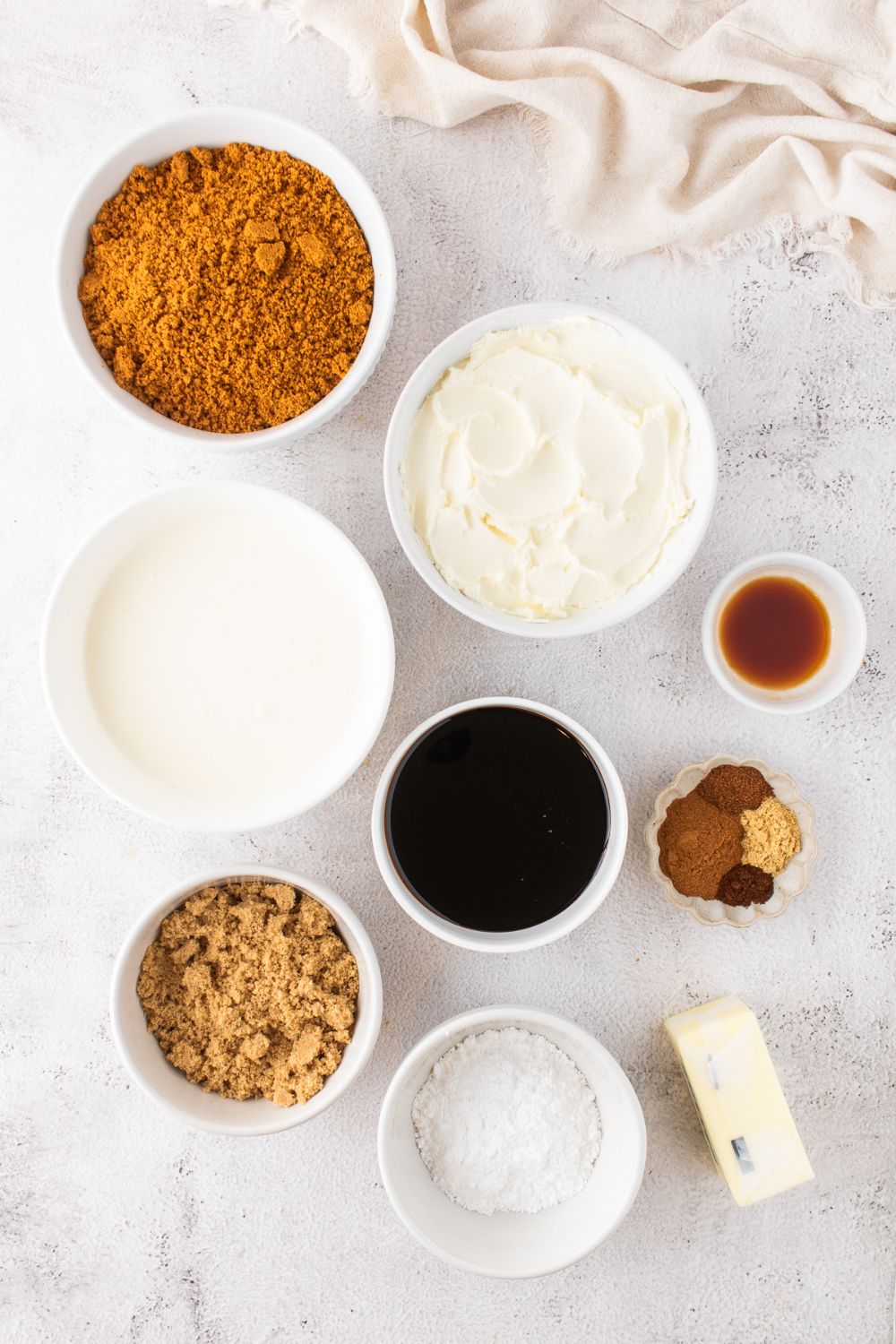 all the ingredients to make No Bake Gingerbread Cheesecake on a white table in small bowls 