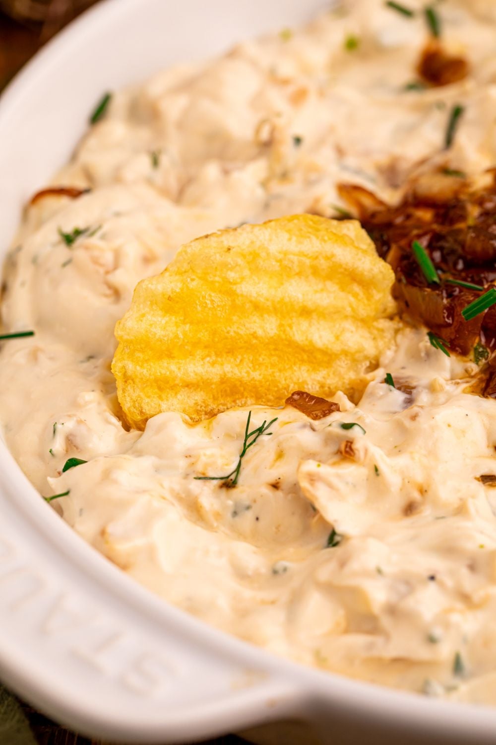 Caramelized Onion Chip Dip in a bowl with a ruffle chip in the bowl 