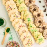 Spritz Christmas Cookies on a long platter with sprinkles and chocolate chips around the table