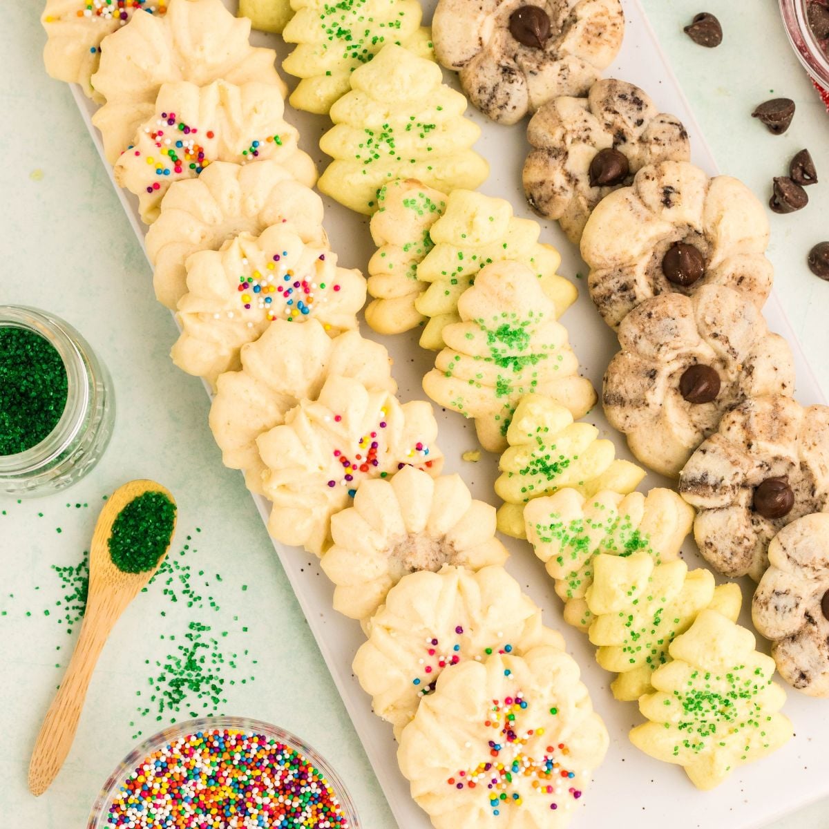 Spritz Christmas Cookies on a long platter with sprinkles and chocolate chips around the table 