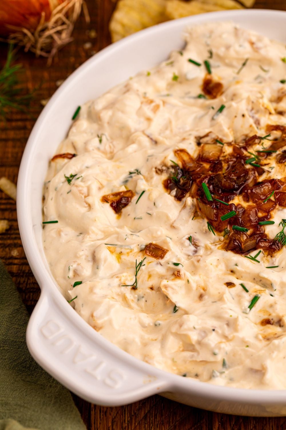 side view of a bowl full of Caramelized Onion Chip Dip with chips behind it on the table 