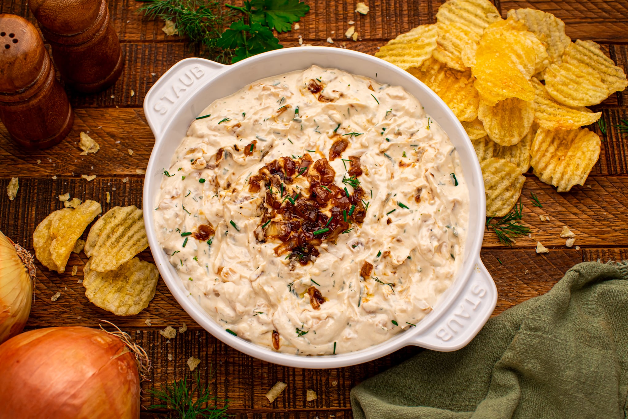 overhead shot of the Caramelized Onion Chip Dip in a white staub bowl on dark wooden table with chips to the side 