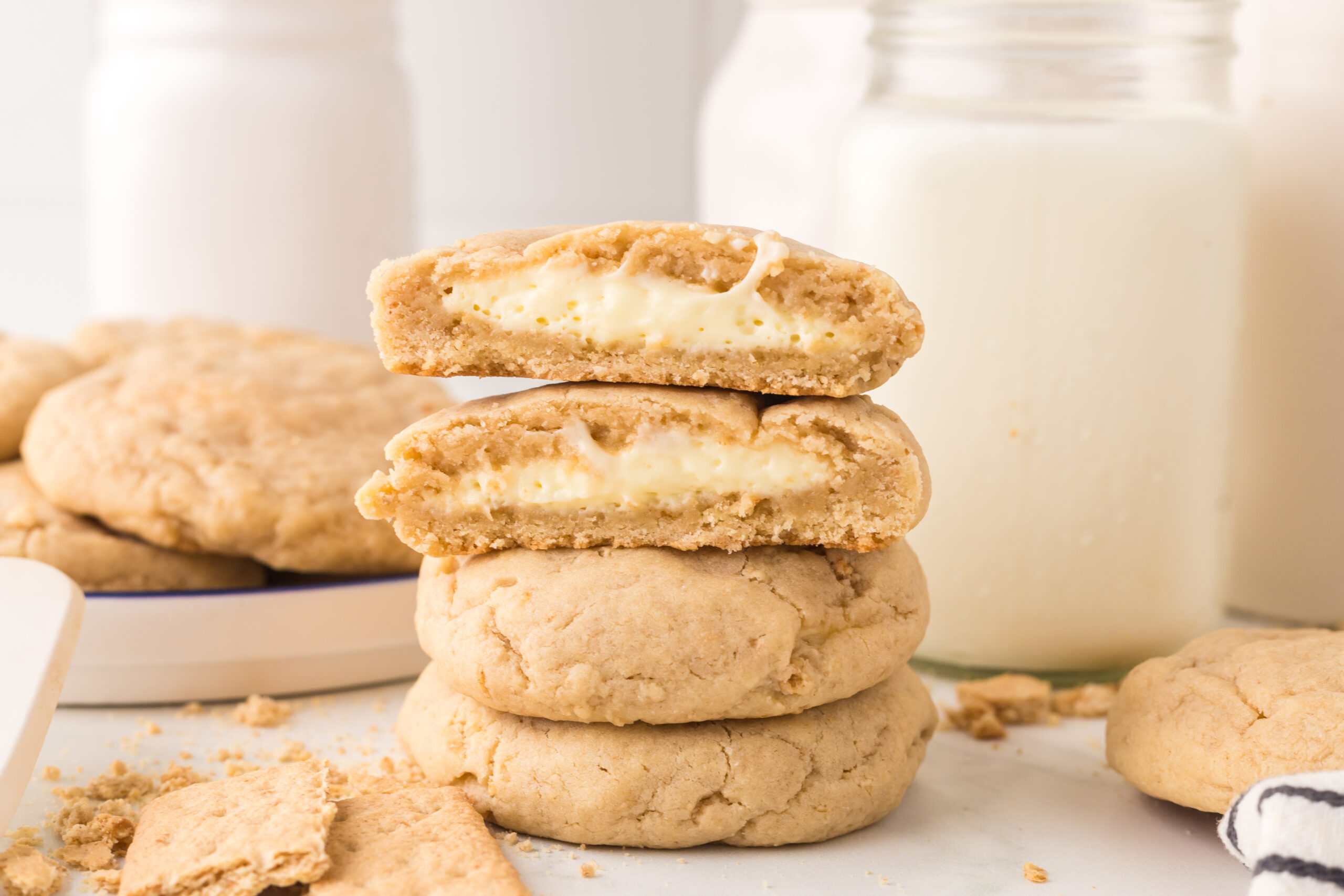 New York cheesecake cookies stacked on top of one another with one cut in half with a glass of milk behind it 