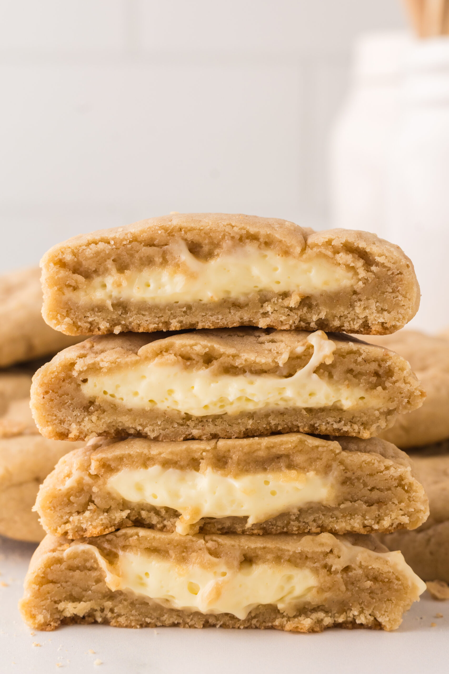 New York cheesecake cookies stacked on top of one another with one cut in half with a glass of milk behind it 