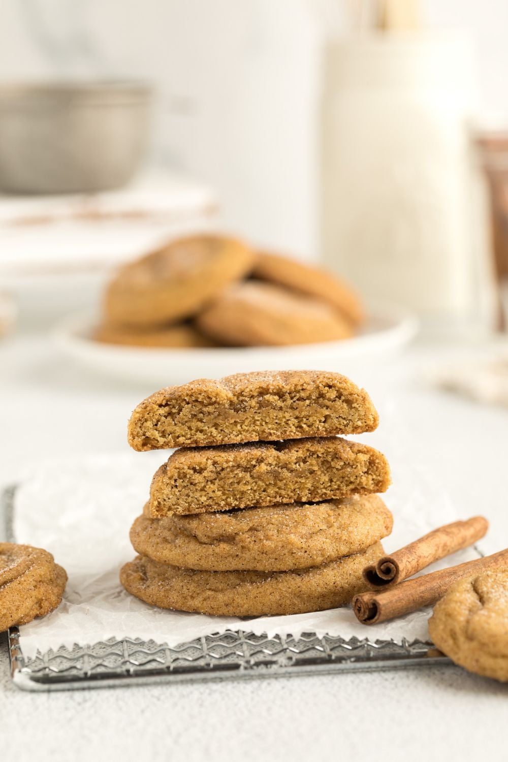 Pumpkin Snickerdoodle Cookies cut in half and placed on top of one another showing the centers of the cookies with a plate and milk behind it farther back on table 