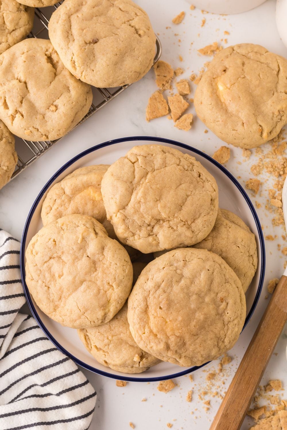 New York cheesecake cookies in a bowl on table with more cookies stacked to side, with graham crackers, towel, and other items around the table 