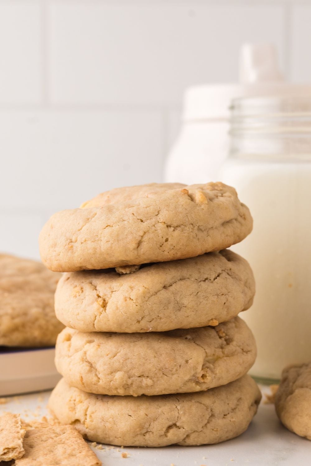 stack of thick cheesecake stuffed cookies on table with a glass of milk behind it and a cutting board with a stack of cookies 