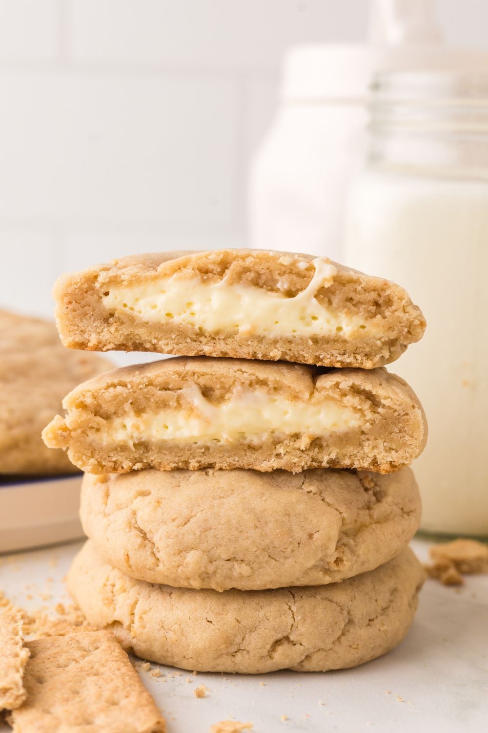New York cheesecake cookies stacked on top of one another with one cut in half with a glass of milk behind it 