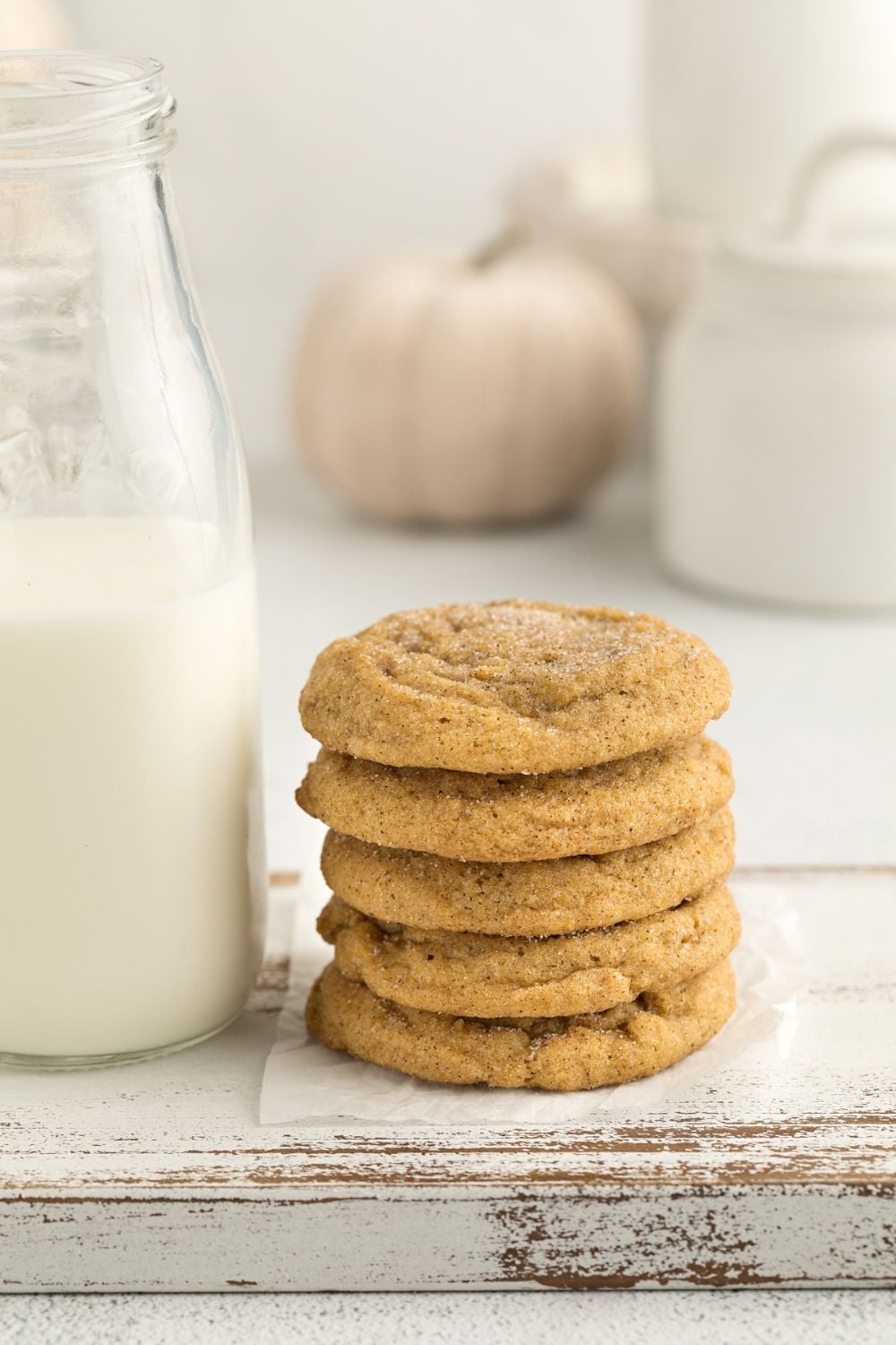 Pumpkin Snickerdoodle Cookies stacked with some milk beside it on table and a white pumpkin in the background 