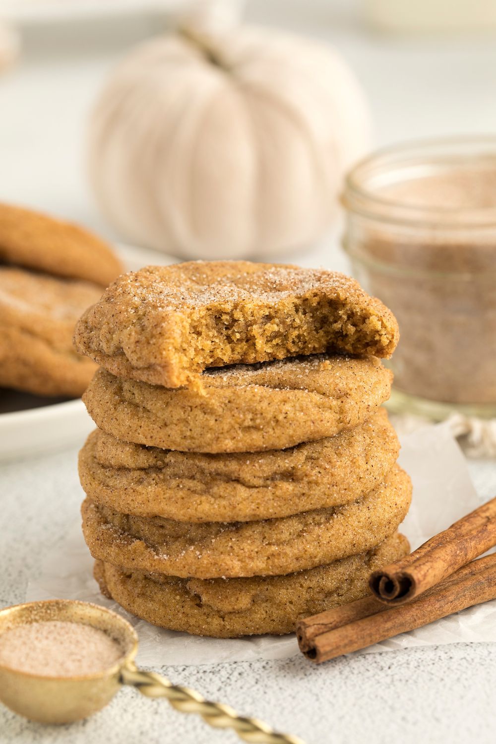 Pumpkin Snickerdoodle Cookies on a plate stacked with the top one with a bite taken out of it and cinnamon sticks to the side of plate 