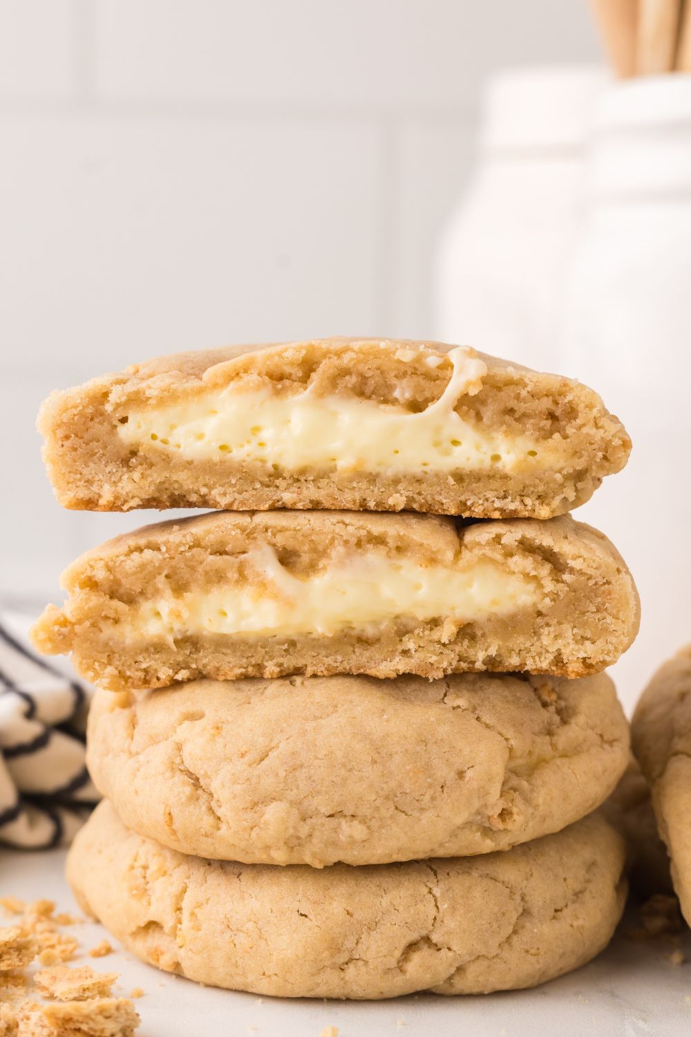New York cheesecake cookies stacked on marble counter with the top cookie cut in half to show it is a stuffed cream cheese cookie 