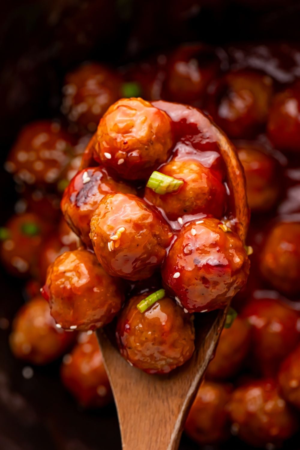 Crockpot Sweet Chili Meatballs in a wooden spoon above the black crockpot full of meatballs 
