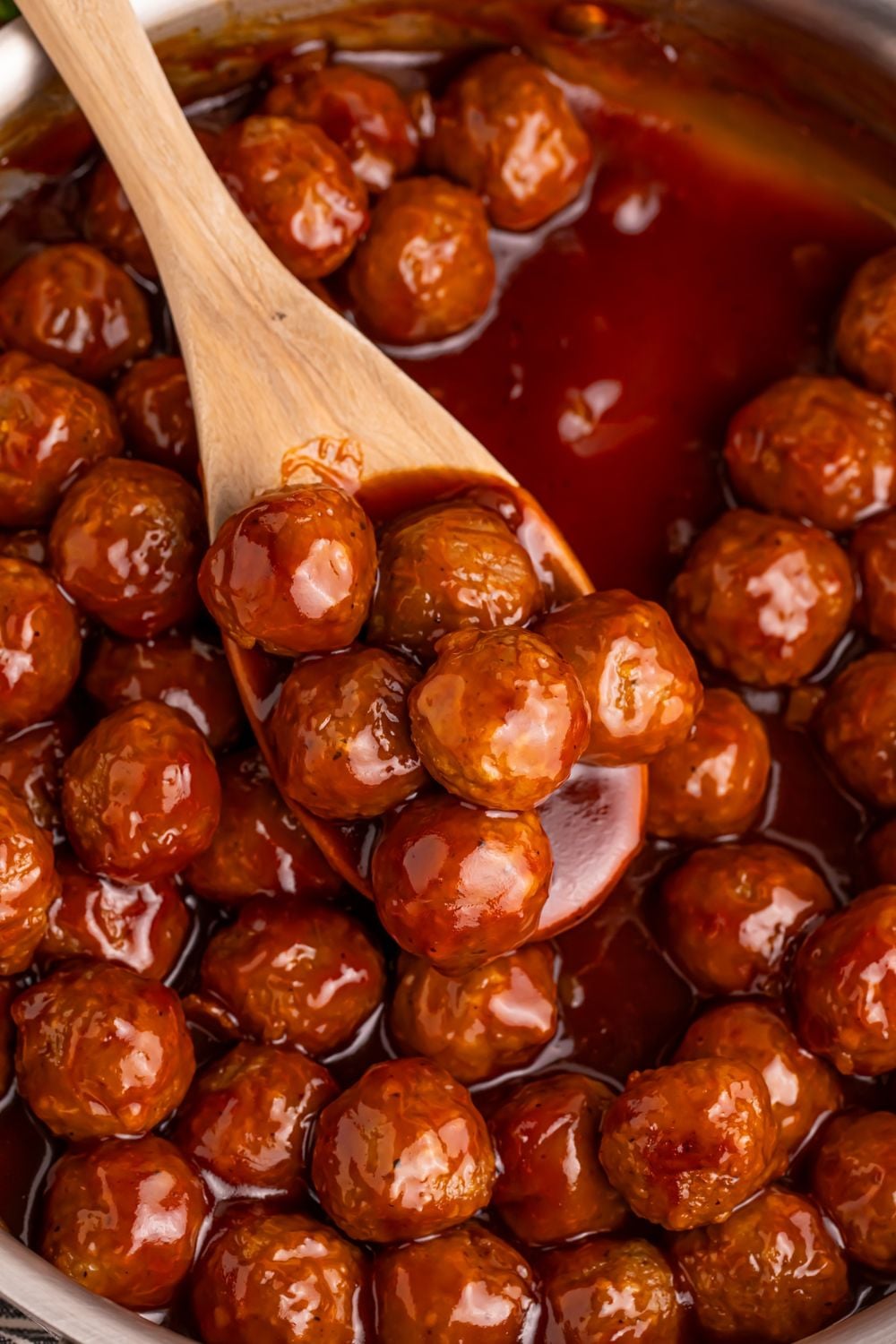Peach BBQ Meatballs in a skillet with a wooden spoon scooping up some of the meatballs 