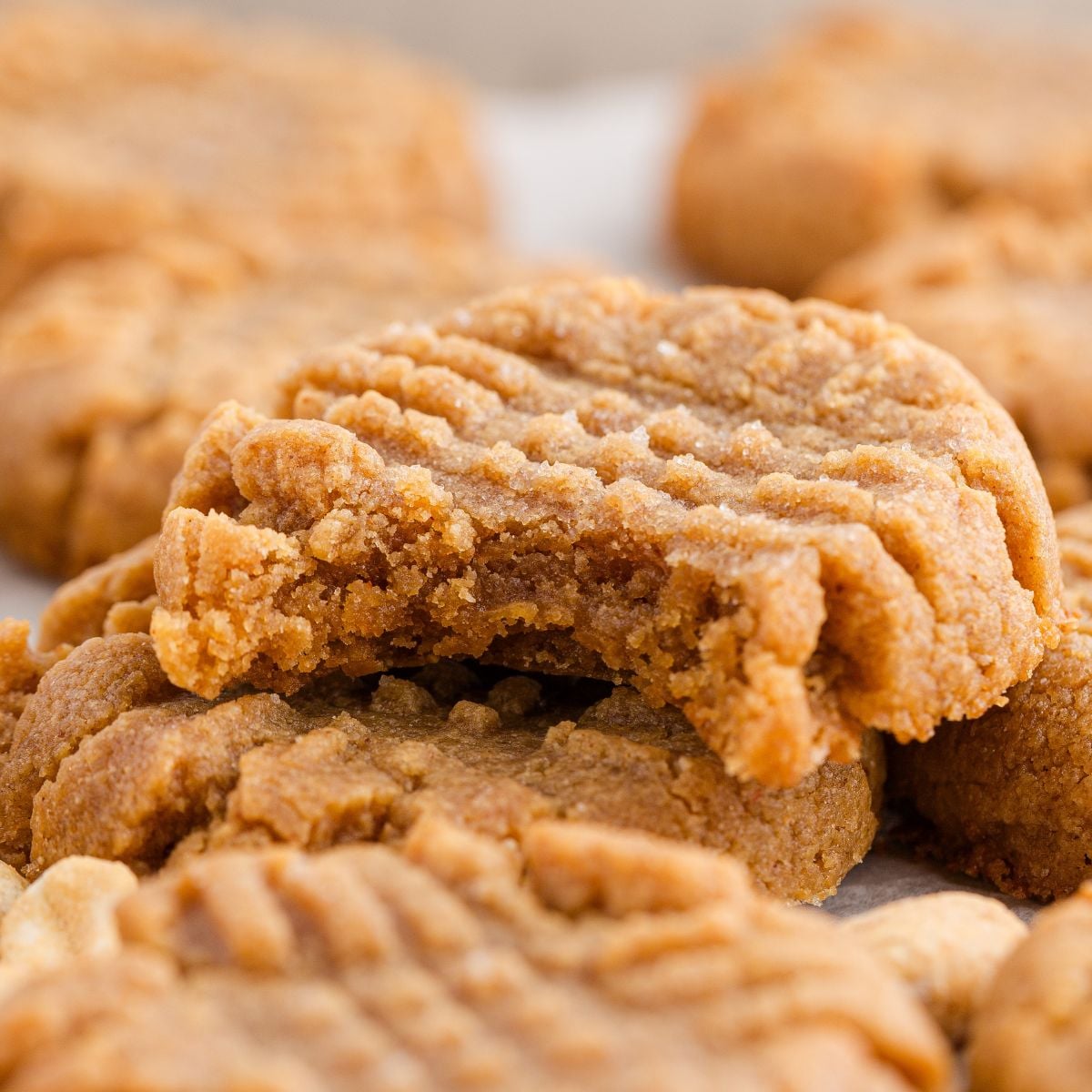 4 Ingredient Peanut Butter Cookies  stacked on a white table with one cookie with a bite taken out of it 