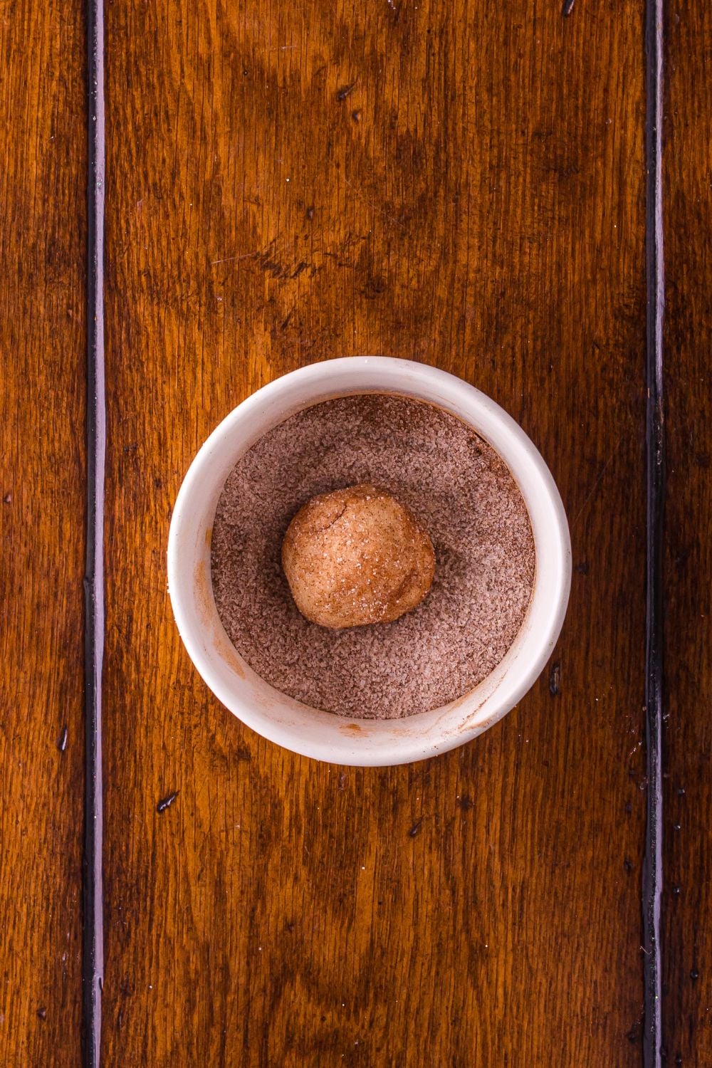 snickerdoodle cookie dough rolled in cinnamon sugar mixture in a white bowl on table 