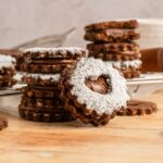 Chocolate Linzer Cookies stacked on the table in piles with one that has a bite taken out of it