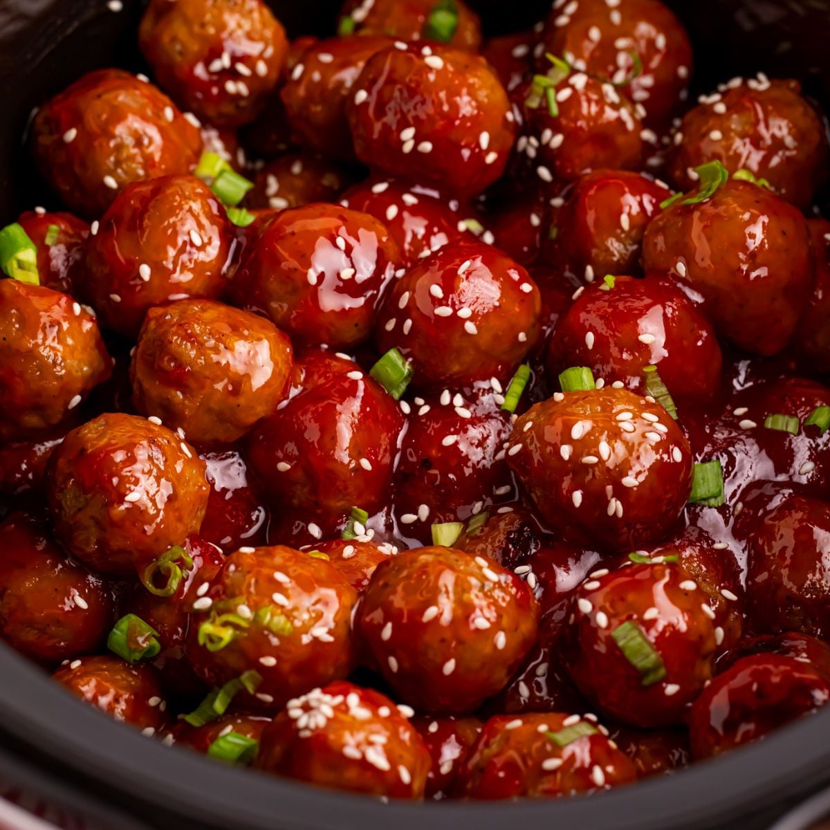 Crockpot Sweet Chili Meatballs in a crockpot on table with sesame seeds sprinkled on top and green onions 