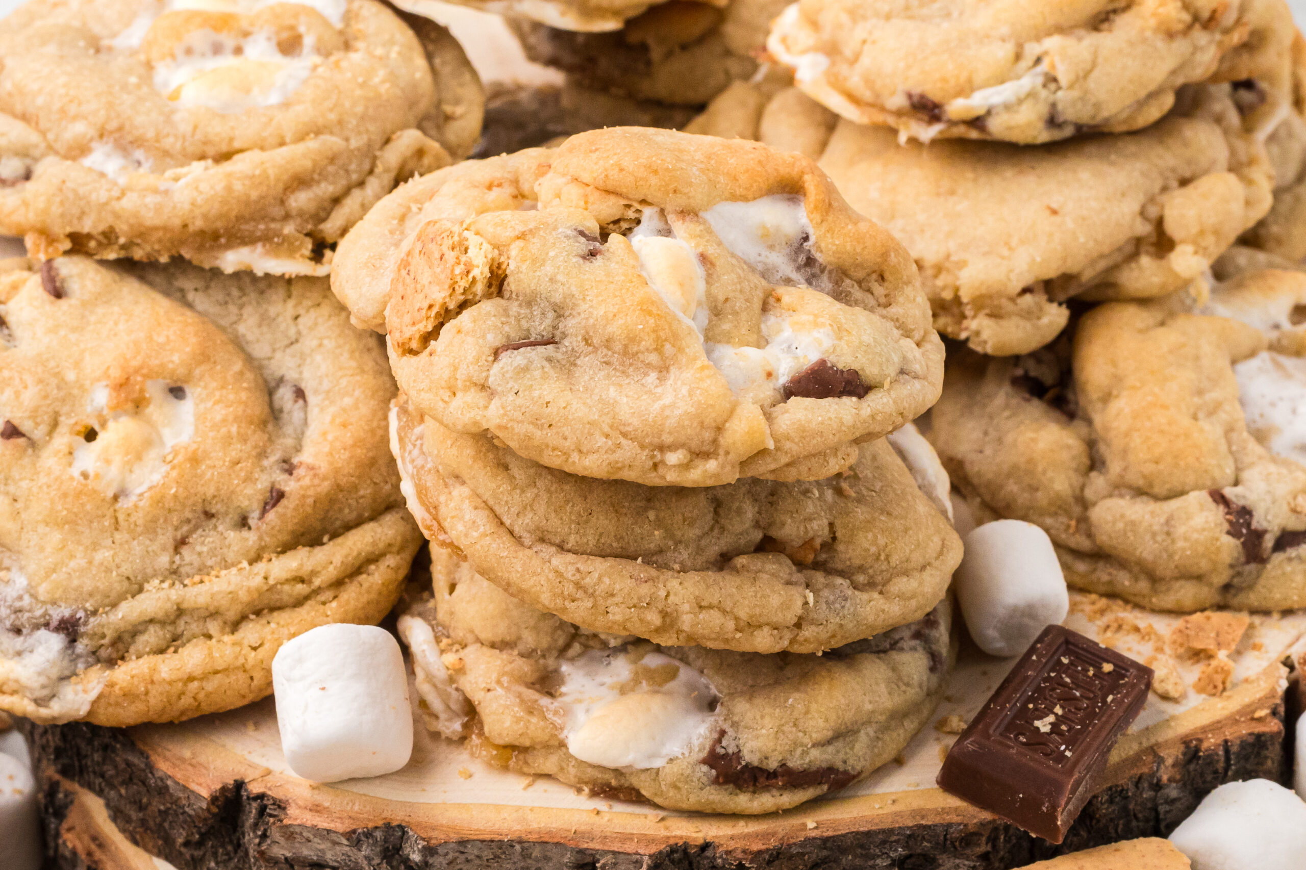 S'mores Cookies stacked on top of one another with marshmallows and chocolate bar pieces around 