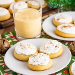 Soft Frosted Eggnog Cookies on plates on a table with a glass of eggnog to the side