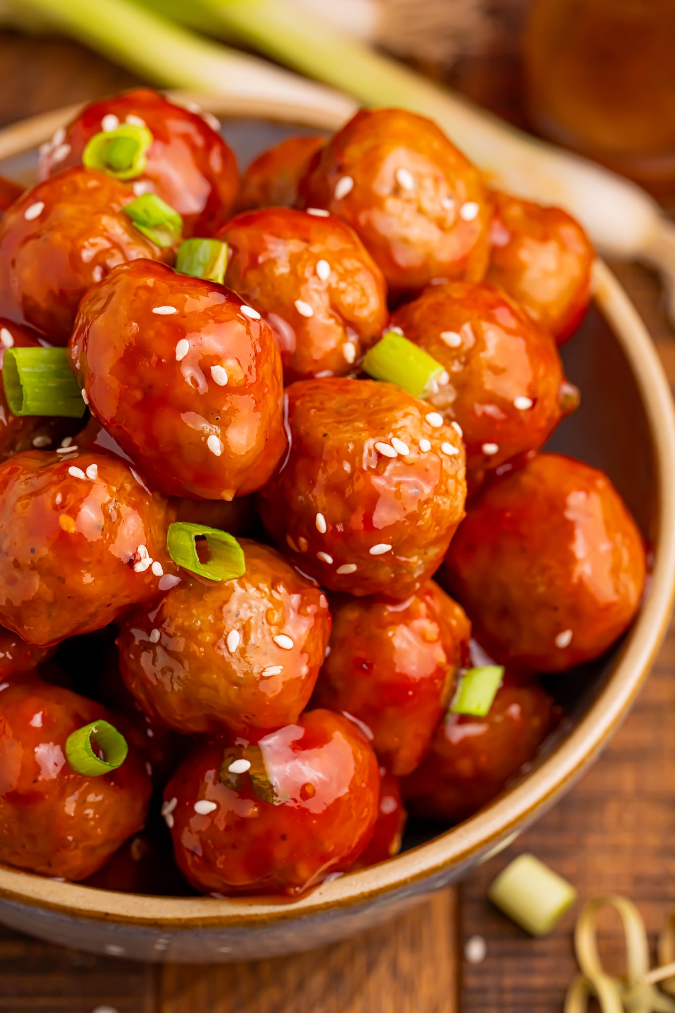 Crockpot Sweet Chili Meatballs in a wooden bowl on table with sesame seeds and green onions sprinkled on top 