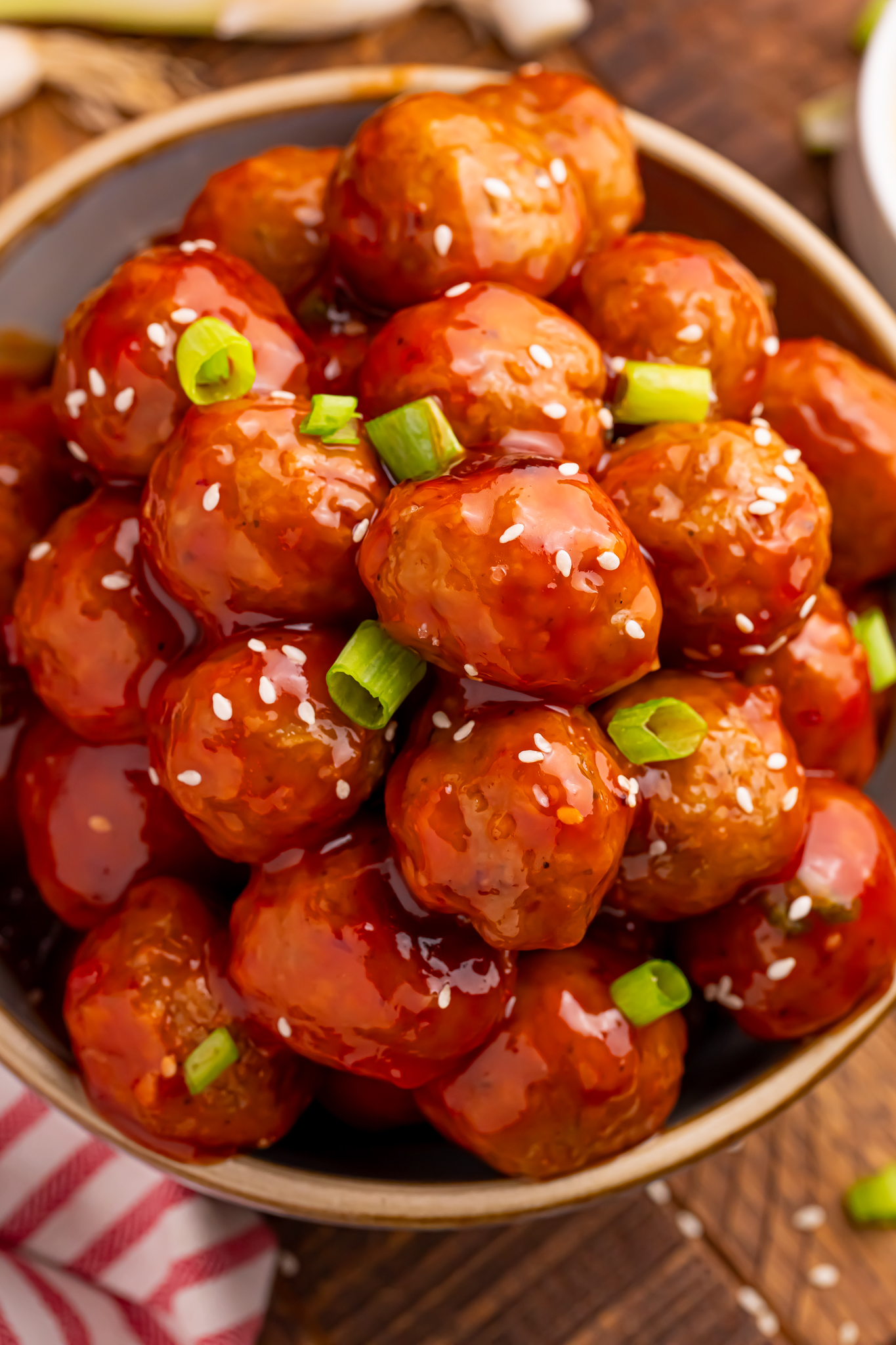 Overhead shot of the Crockpot Sweet Chili Meatballs in a wooden bowl on table with sesame seeds and green onions sprinkled on top 