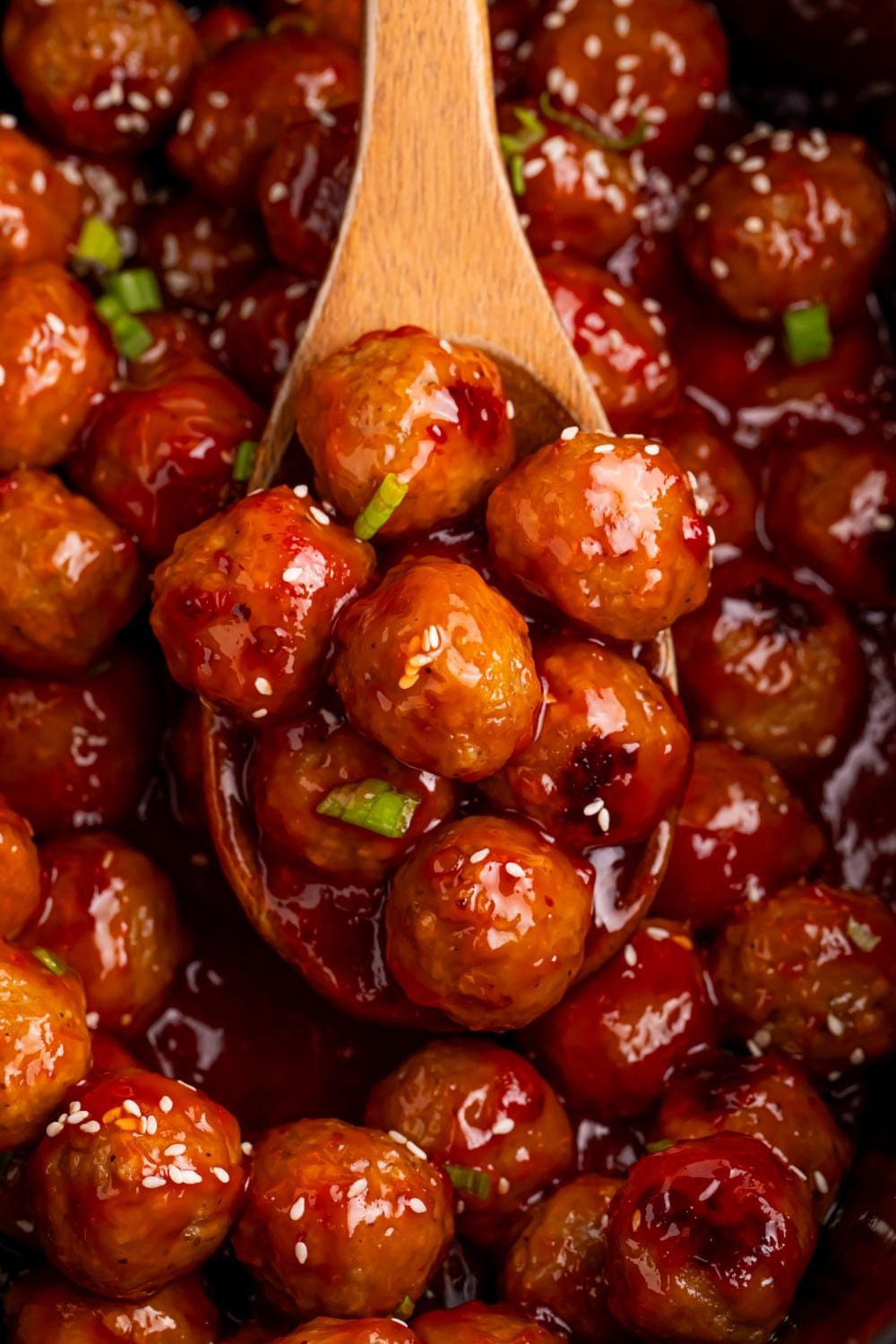Crockpot Sweet Chili Meatballs in a crockpot with sesame seeds and a wooden spoon full of meatballs 