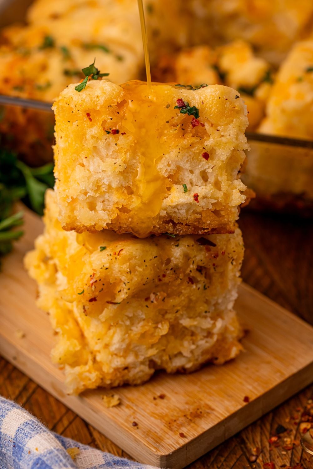 Cowboy Butter Swim Biscuits stacked on a wooden cutting board with some cowboy butter pouring over the biscuits 