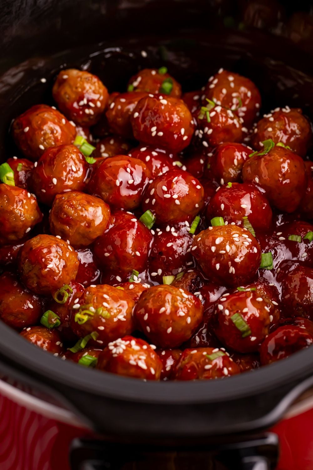 close up of Crockpot Sweet Chili Meatballs in a slow cooker on table topped with chopped green onions and sesame seeds 