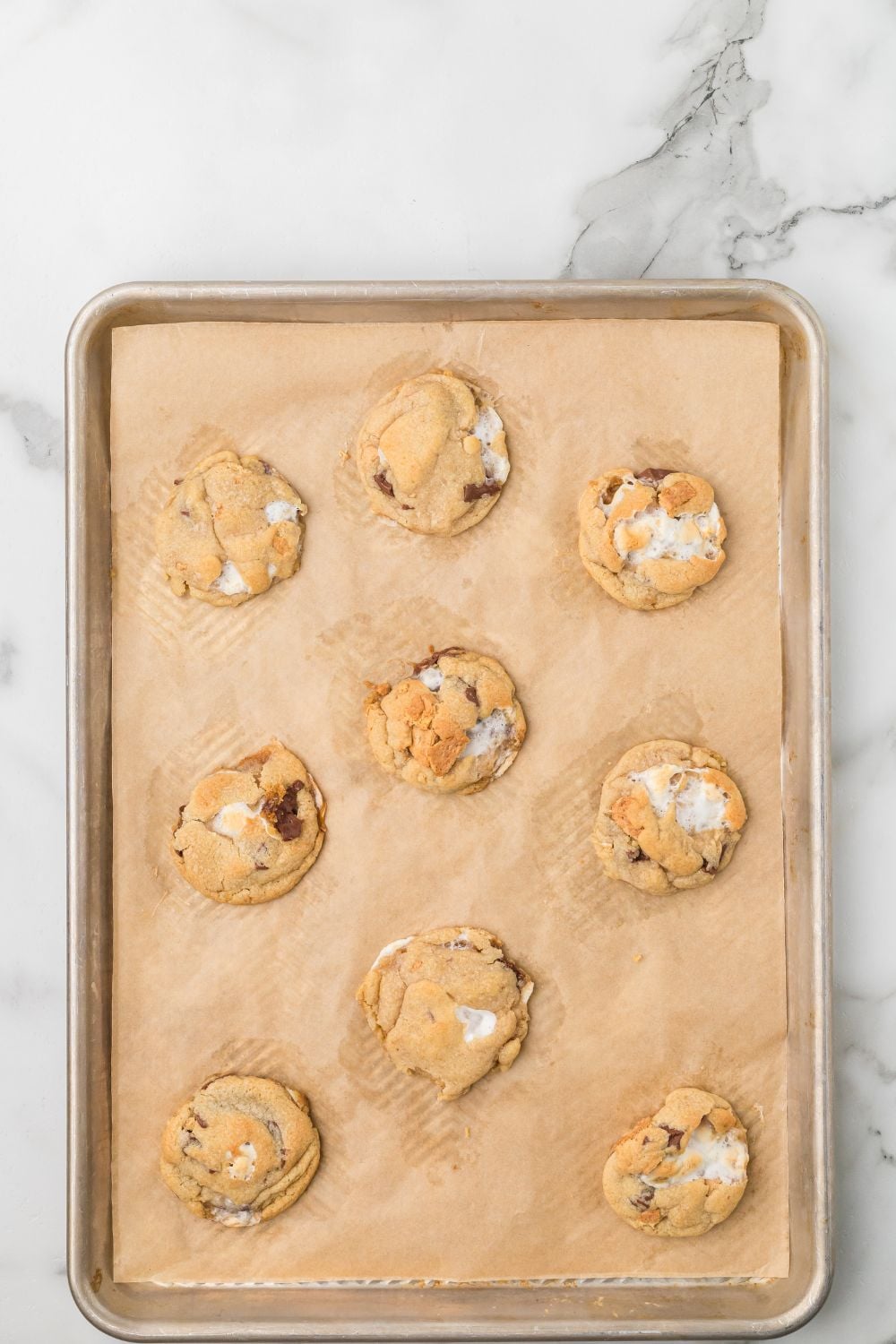 baked S'mores Cookies on a cookie sheet with parchment paper sitting on marble counter 