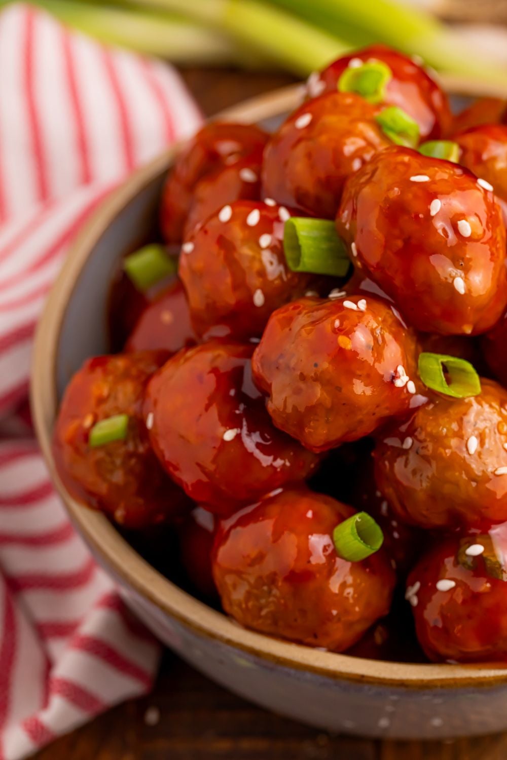 close up of Crockpot Sweet Chili Meatballs in a bowl with a red striped towel laying beside the table 