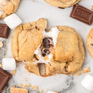 gooey s'mores cookies spread out on table with one pulled apart showing melted marshmallow