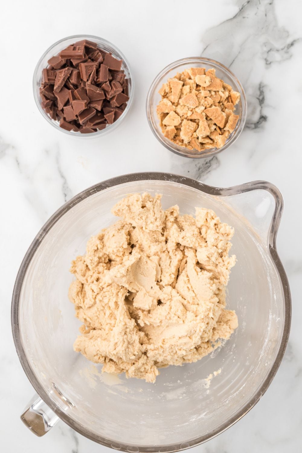 glass bowl  for smore cookies on table with a bowl of crushed graham crackers and chocolates to side 