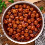 Peach BBQ Meatballs in a skillet on a wooden table with parsley to the side of it