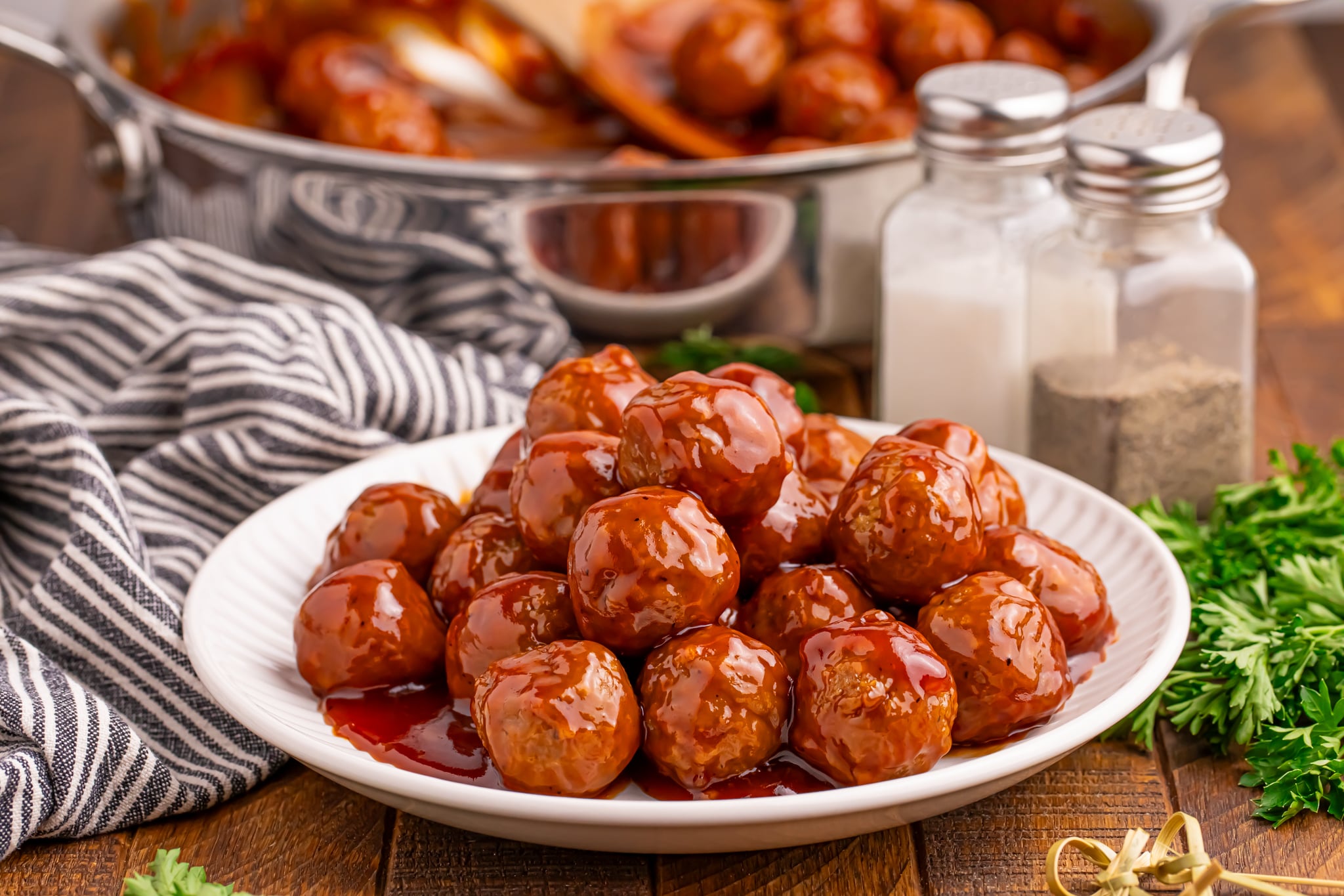 Peach BBQ Meatballs on a white plate on a dark wooden table with a skillet behind the plate
