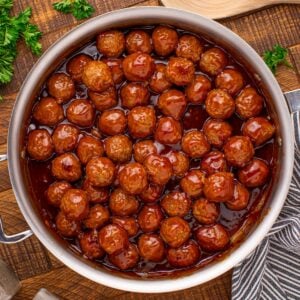 Peach BBQ Meatballs in a skillet on a wooden table with parsley to the side of it
